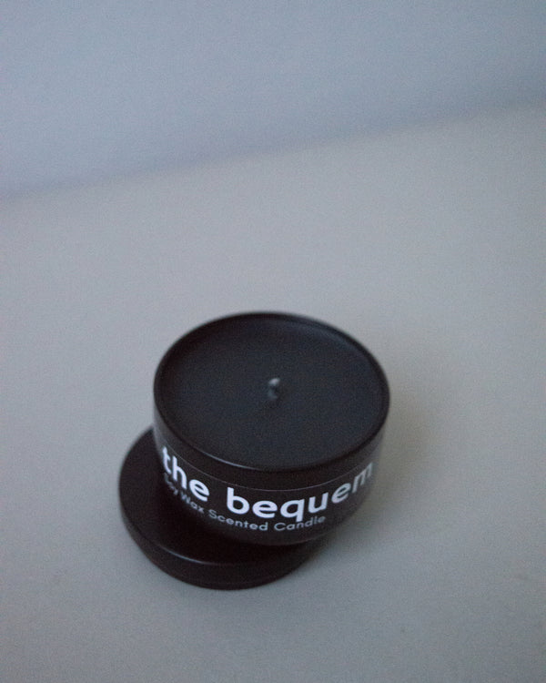 Soy wax travel candle by The Bequem in matte black metal tin with lid on light grey background.