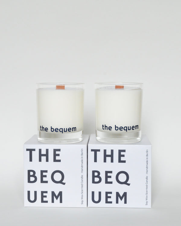 Two soy candles with white wax, clear glass containers, and wooden wicks, placed on boxes with the brand name 'THE BEQUEM'.