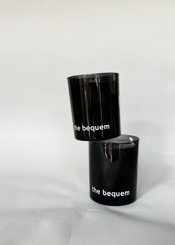 Two black soy candles with ‘the bequem’ logo, stacked on a soft white fabric background