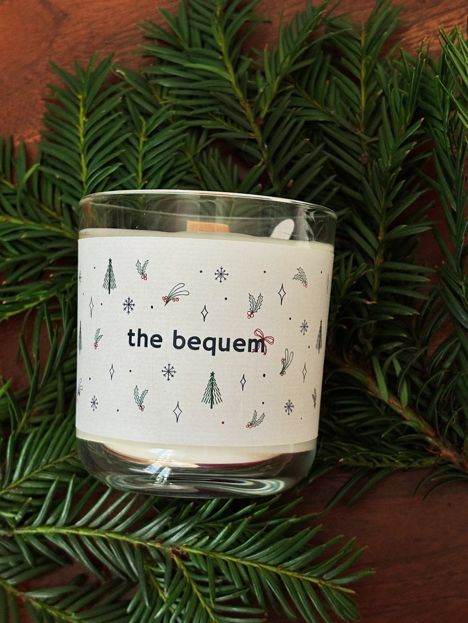 Candle with 'the bequem' label on a bed of green pine needles