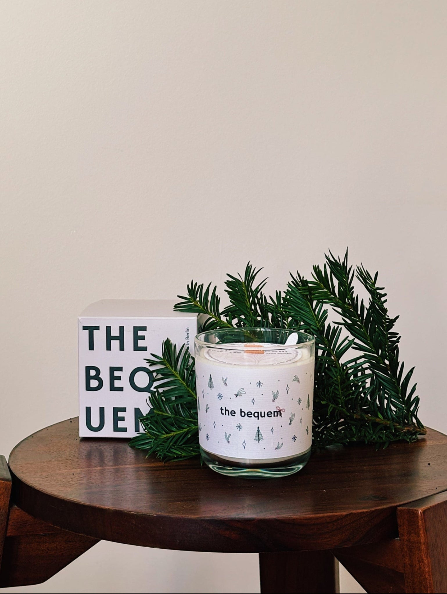 Candle with greenery on a wooden stool against a beige wall