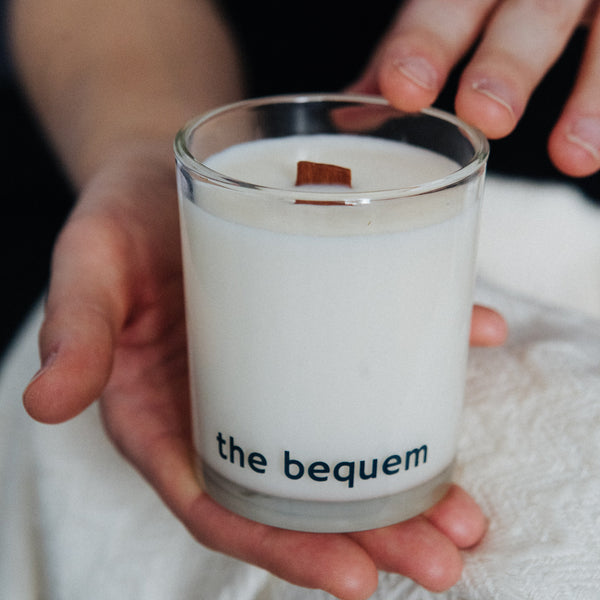 Hand-poured Fruits soy wax candle by The Bequem with wooden wick in clear glass jar held in hands on soft white fabric background