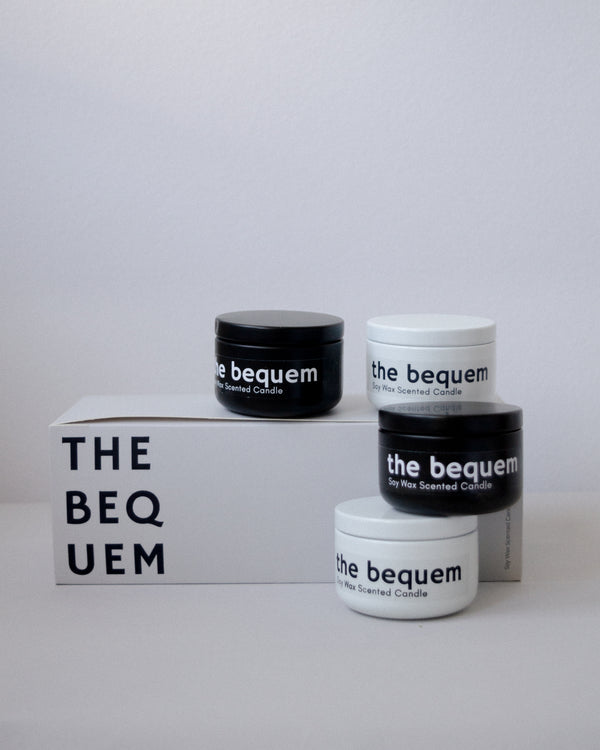 Set of four The Bequem soy wax travel candles in black and white tins stacked on minimalist display box with brand logo